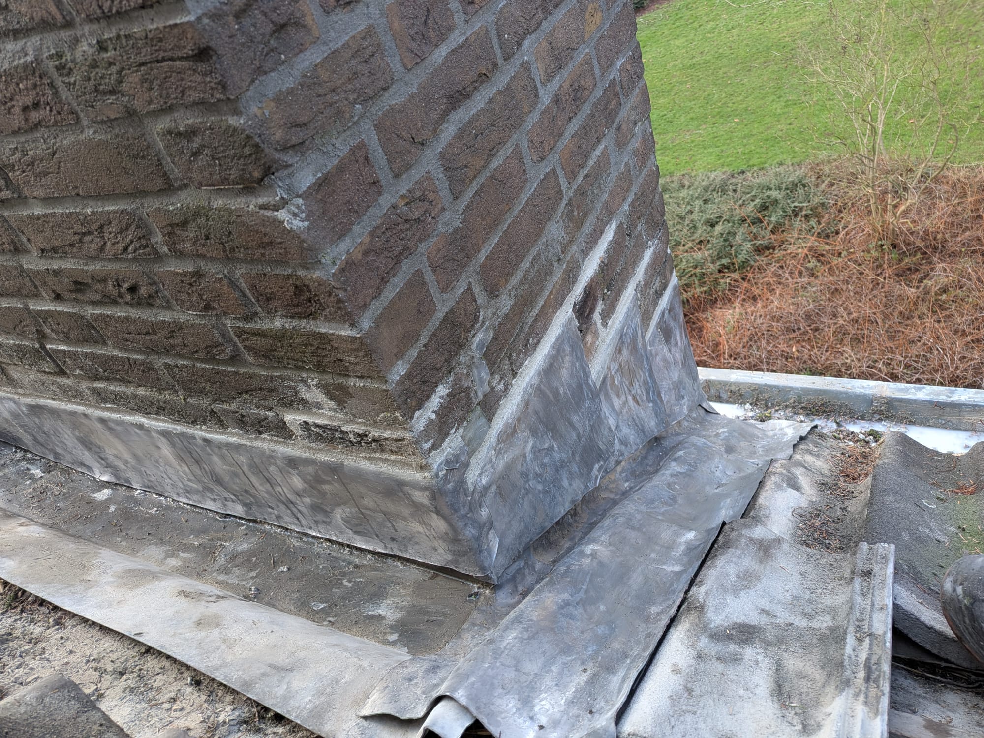Metselwerk schoorsteen met loodslabben op dak.